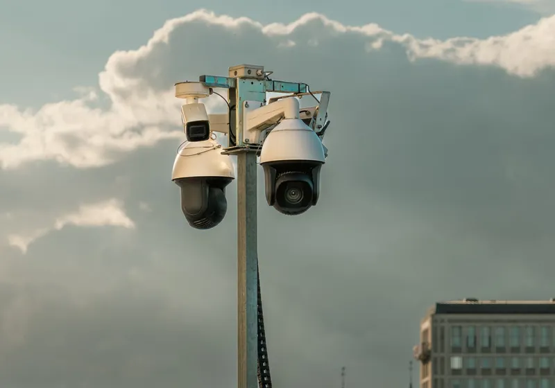 Twee bewakingscamera's hoog op een paal, afgetekend tegen een bewolkte lucht